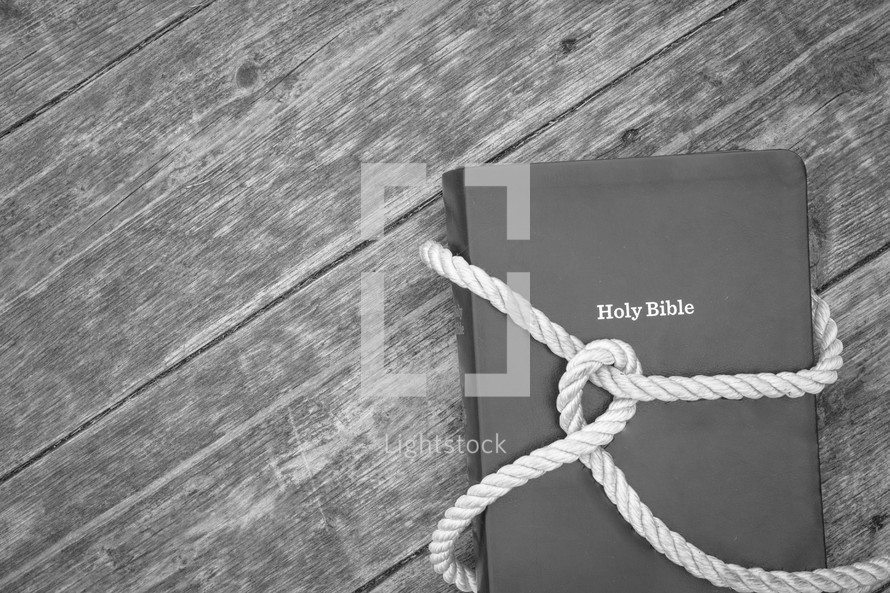 knot in rope around a Bible on a wood background 