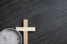 Small wood cross and bowl of ashes on dark wood