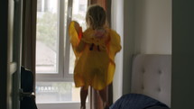Little girl wearing a yellow poncho jumping on the bed