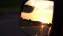 Driving POV through the rear view mirror at sunrise 