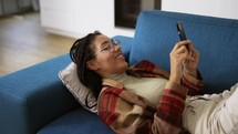 Happy African American girl relaxing on sofa at home with smartphone.