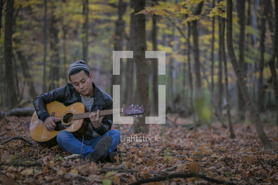 a man sitting in a forest playing a guitar 