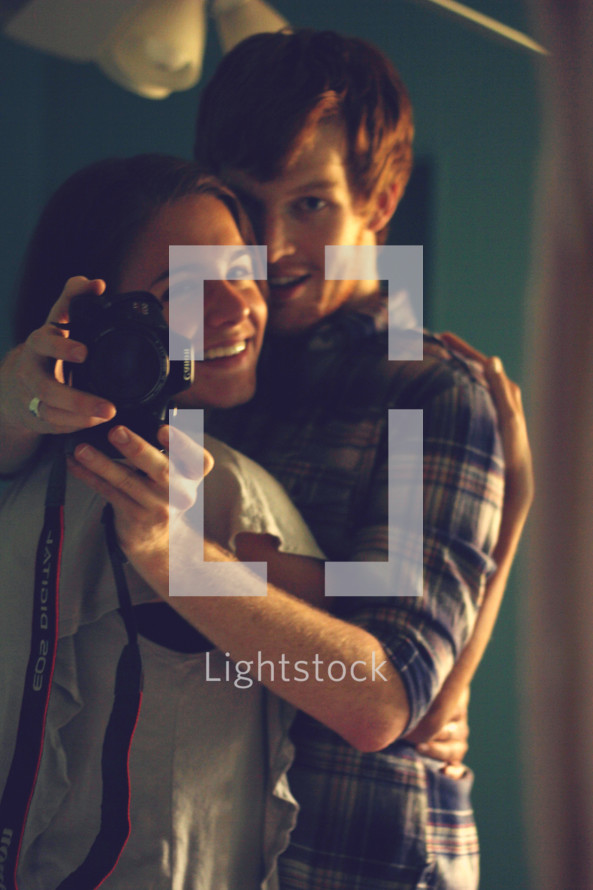 a couple holding a camera hugging 