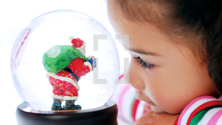 toddler girl looking at a Santa snow globe 