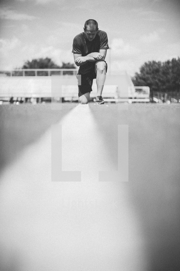 man kneeling in prayer on a football field 