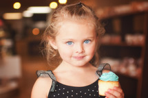 a young girl holding a cupcake with blue icing 