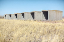 Row of cement storage containers in a field.