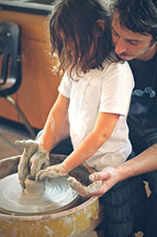 A father helping his daughter create a bowl on the potters wheel.