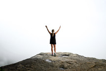 a woman standing with hands raised on a mountaintop 