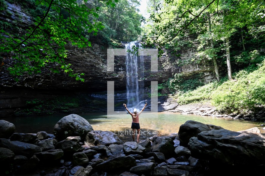 a woman with raised hands and a waterfall in a forest 