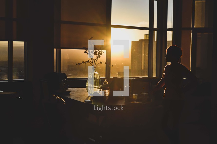person standing at a table in an apartment at sunset 