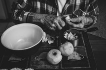 elderly woman sitting at a kitchen table peeling apples 