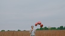a woman with red balloons walking through a field 