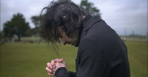Young man in black suit praying in worship in cinematic slow motion.