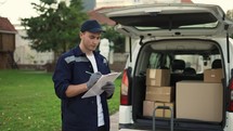 Young delivery man checking list. Delivery man in cap and documentation in hands. Courier with parcel. Male beautiful courier checks the parcels against the delivery list.
