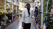 African American man walking along shelves in hardware store and examines goods.
