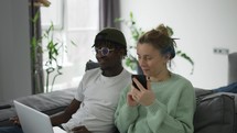 Happy biracial couple sitting on sofa with laptop and cellphone, congratulating each other.
