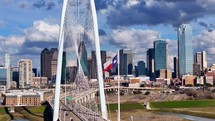 Texas Flag waving in the wind with Margaret Hunt Hill bridge and Dallas skyline in the background