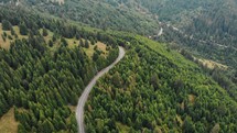 Aerial drone shot of cars driving on a country road in a mountain forest.