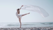  Young beautiful ballerina dancing ballet on seashore with huge silk fabric fluttering in wind.Concept of tenderness, lightness, art and talent in nature.