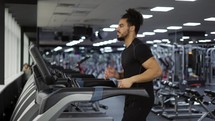 Fitness man training cardio exercise on running machine in gym, side view.