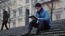 a man sitting on city steps reading a Bible 