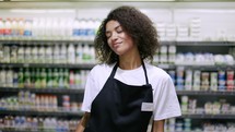 Smiling worker in black apron dancing in supermarket, having fun during work.