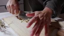 Hands Cut Garlic Into Small Pieces Using A Knife - Close Up