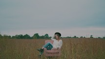a woman walking through a field of tall grasses and sitting in a chair 