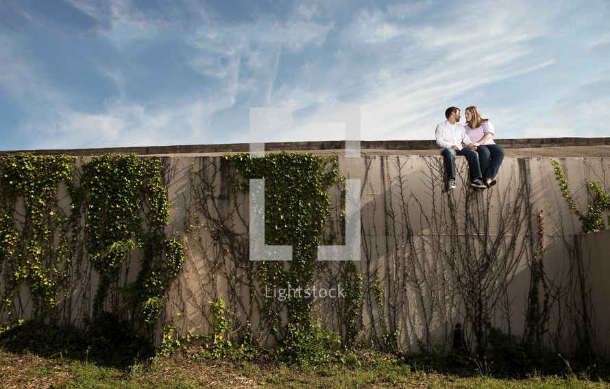 man and woman sitting on an ivy covered wall