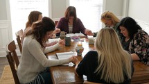 women holding hands in prayer at a women's group Bible study sitting around a table 