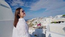 A beautiful tourist woman enjoying view at the blue domed church of the village of Oia, Santorini, Greece, during her summer holidays
