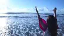 woman standing in the ocean with raised hands 