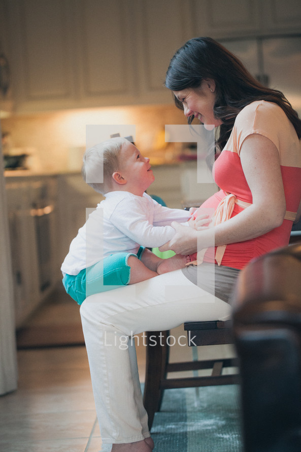 Mother holding son on her lap while sitting in a kitchen chair.