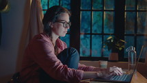 Young tired woman taking off eyeglasses, rubbing her eyes and using laptop at home, working overtime at night before the deadline. Medium shot
