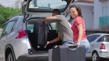 Happy couple puts his suitcase in the back of the car and prepares to leave for trip. Husband and wife open the back of the car put luggage travel. Couple moving into new home at moving day
