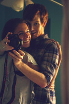 a couple holding a camera hugging 