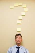 Businessman sitting underneath post it notes in the shape of a question mark