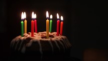A bundt cake in a dark space with candles. The candles are lit and then blown out
