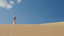 Traveler woman leaving footprints on sand dune at golden sunset.
