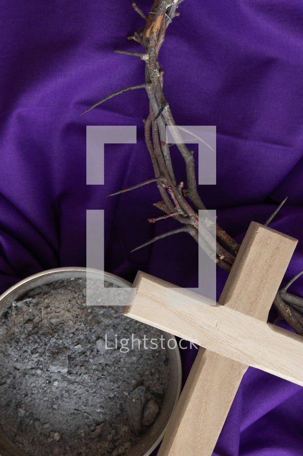 Wood cross, crown of thorns and bowl of ashes on a purple cloth background with copy space