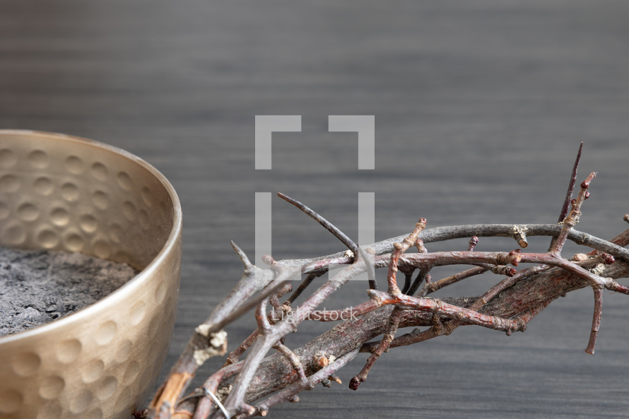 Partial crown of thorns and bowl of ashes on a dark wood background with copy space