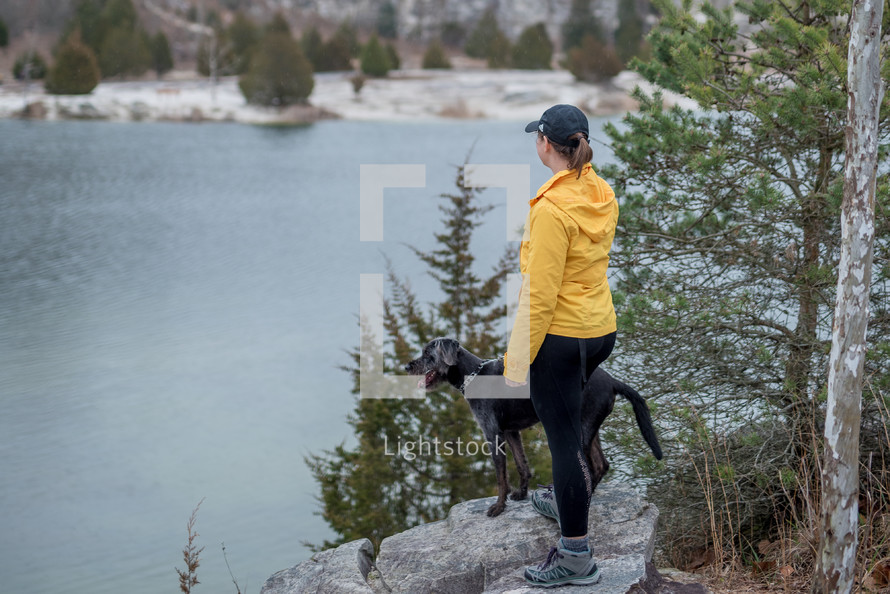 a woman and her dog looking out at a lake 