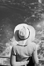 a woman in a hat looking out at the ocean 