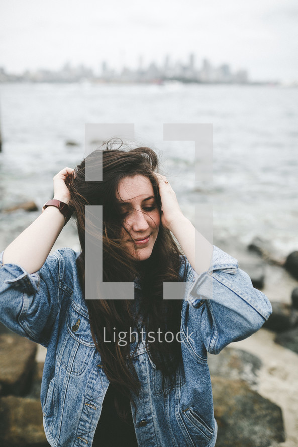 a woman standing on a rocky shore with hair blowing in the breeze 