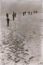 people walking on a beach leaving tracks in the sand 