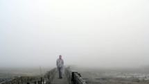 man walking on a boardwalk on a foggy morning 