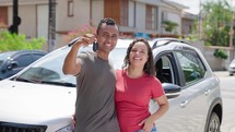 Young hispanic couple smiling and kissing confident holding key of new car at street

