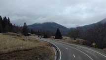 Aerial drone shot of an empty concrete road through sloping mountains under a gloomy sky.