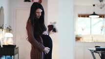 expectant mother holding her pregnant belly standing in her home 